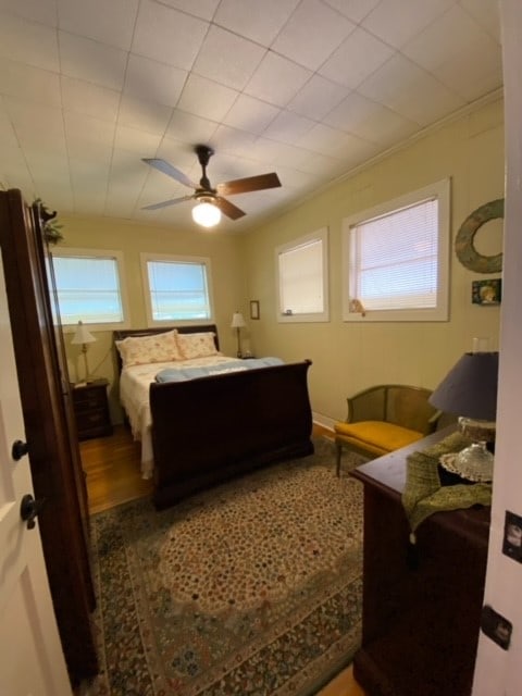 bedroom with ceiling fan, multiple windows, crown molding, and wood-type flooring