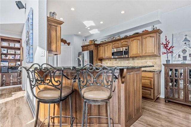 kitchen featuring light stone countertops, appliances with stainless steel finishes, light wood-type flooring, and a breakfast bar