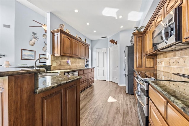 kitchen with sink, tasteful backsplash, dark stone counters, appliances with stainless steel finishes, and hardwood / wood-style flooring