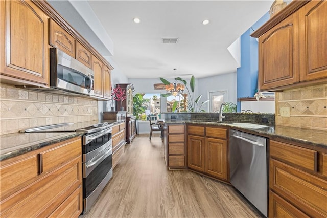 kitchen with backsplash, dark stone countertops, light wood-type flooring, and stainless steel appliances