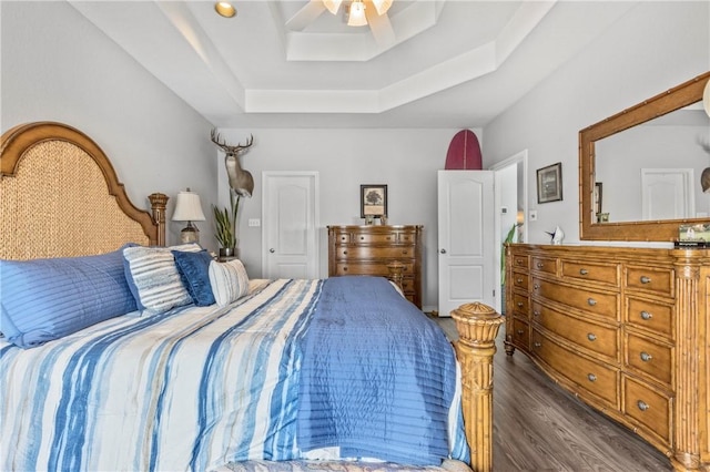 bedroom with a tray ceiling, ceiling fan, and dark wood-type flooring