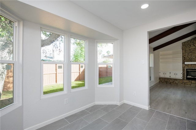 interior space with a stone fireplace, hardwood / wood-style flooring, and vaulted ceiling with beams