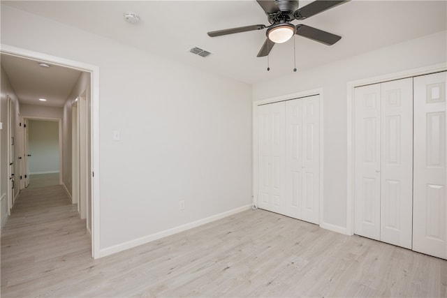 unfurnished bedroom with ceiling fan, light hardwood / wood-style flooring, and two closets