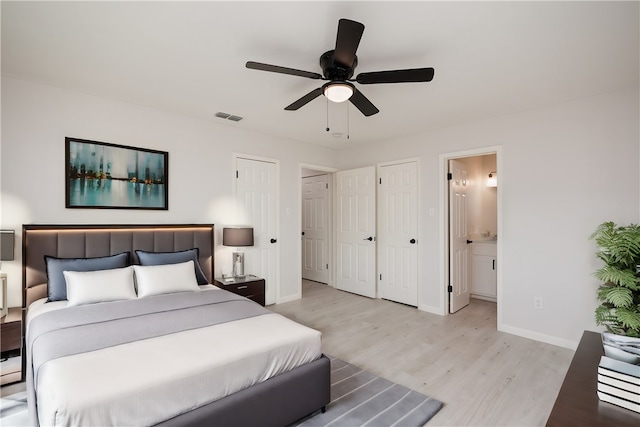 bedroom featuring multiple closets, light hardwood / wood-style flooring, ceiling fan, and connected bathroom