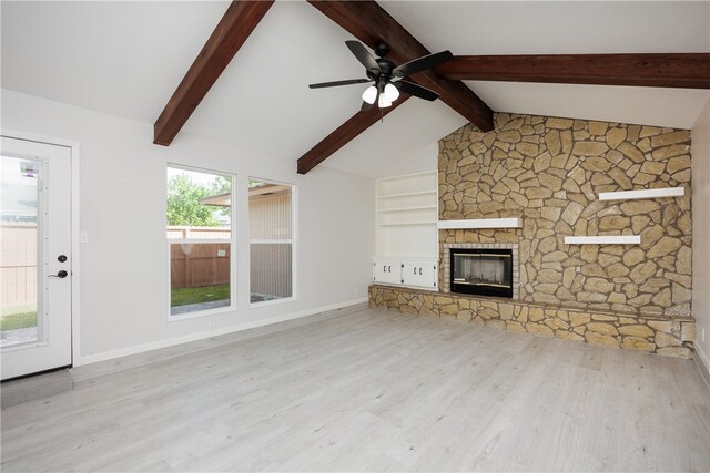 unfurnished living room with ceiling fan, light hardwood / wood-style floors, a stone fireplace, and lofted ceiling with beams