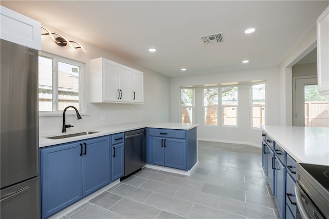 kitchen with white cabinets, kitchen peninsula, sink, blue cabinetry, and appliances with stainless steel finishes