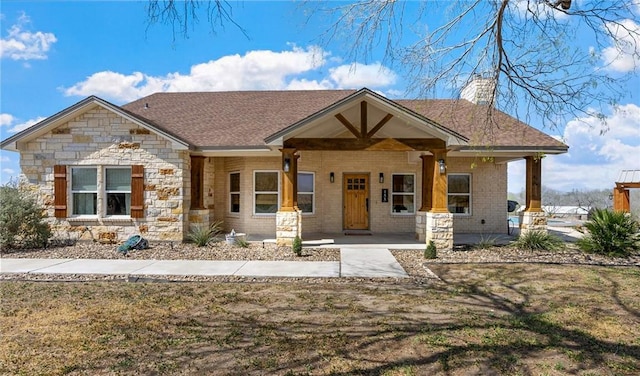 craftsman house featuring roof with shingles, a porch, a chimney, and brick siding