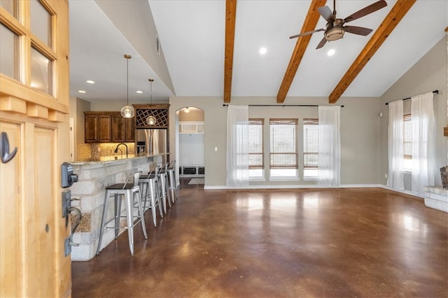 living room featuring vaulted ceiling with beams, a ceiling fan, baseboards, and concrete flooring