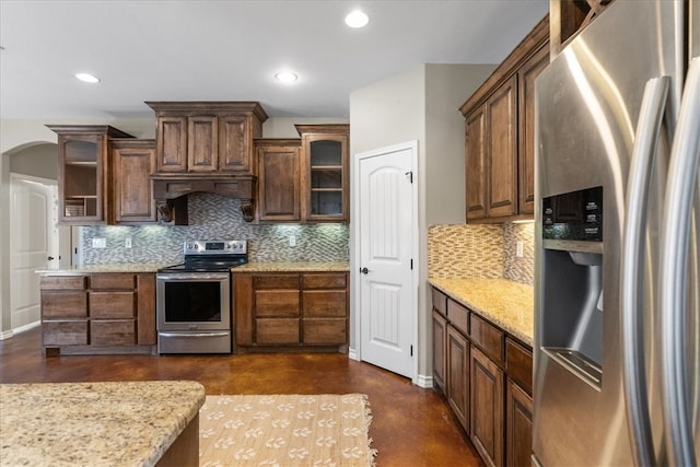 kitchen featuring appliances with stainless steel finishes, arched walkways, glass insert cabinets, and tasteful backsplash