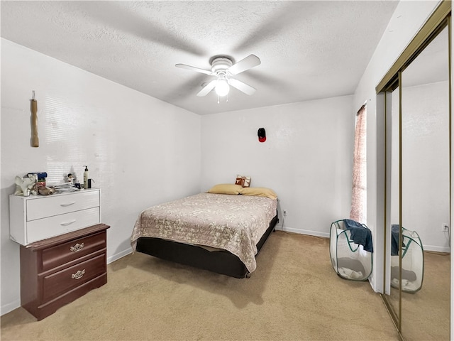 bedroom with a textured ceiling, a closet, ceiling fan, and light colored carpet