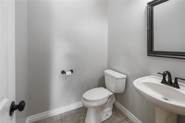 half bath with baseboards, a sink, tile patterned floors, and toilet