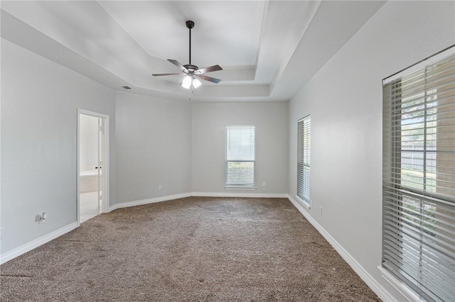 unfurnished room featuring carpet floors, a tray ceiling, baseboards, and ceiling fan