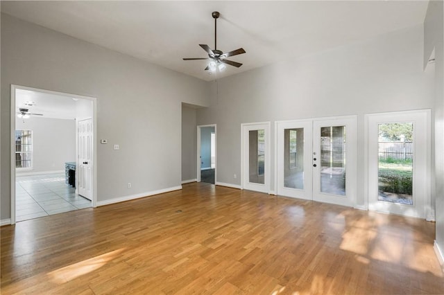 unfurnished living room with french doors, a ceiling fan, light wood-type flooring, baseboards, and a high ceiling