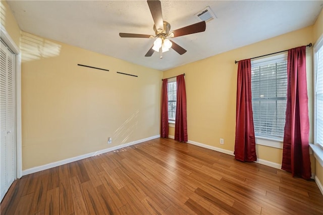 empty room featuring wood finished floors, baseboards, ceiling fan, and visible vents
