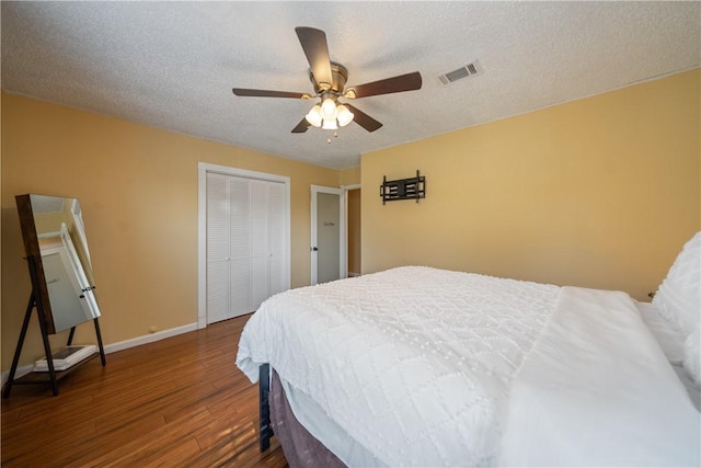 bedroom with a closet, a textured ceiling, visible vents, baseboards, and wood finished floors