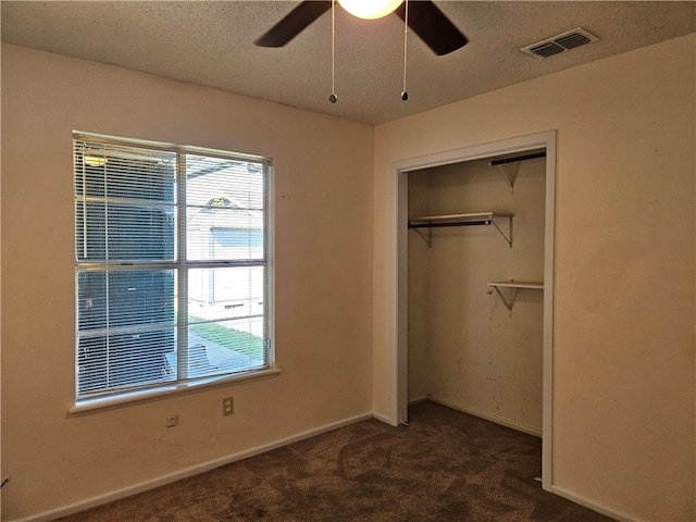 unfurnished bedroom with ceiling fan, a textured ceiling, a closet, and dark carpet