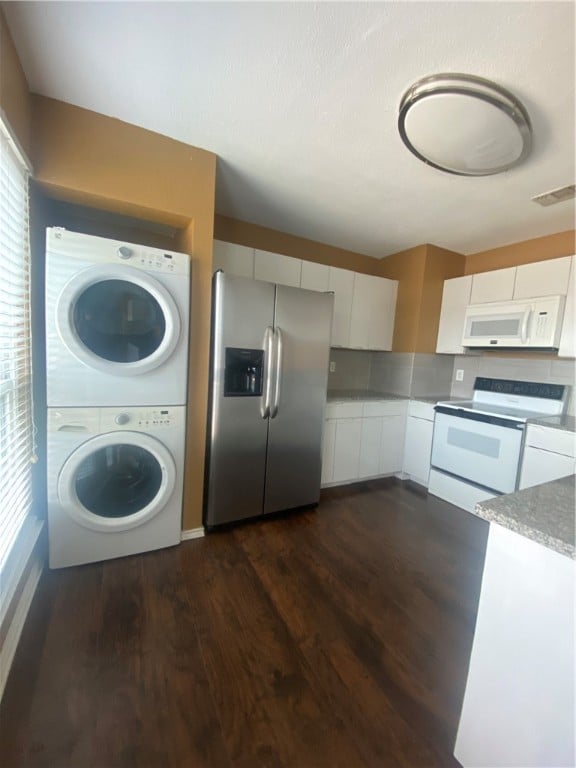 kitchen featuring stacked washer / drying machine, white cabinetry, white appliances, and dark wood-type flooring