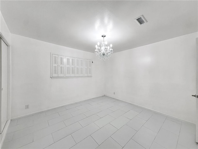 unfurnished room featuring baseboards, visible vents, and an inviting chandelier