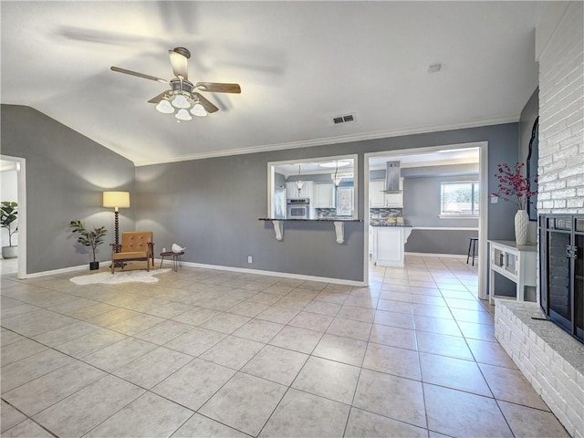 interior space featuring a brick fireplace, ornamental molding, ceiling fan, light tile patterned floors, and lofted ceiling