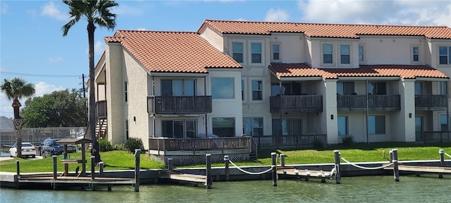 back of property with a water view, a yard, and a balcony