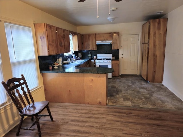 kitchen featuring white range with gas cooktop, decorative backsplash, sink, dark hardwood / wood-style floors, and kitchen peninsula