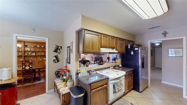 kitchen with light tile patterned floors, visible vents, stainless steel fridge, white electric stove, and under cabinet range hood