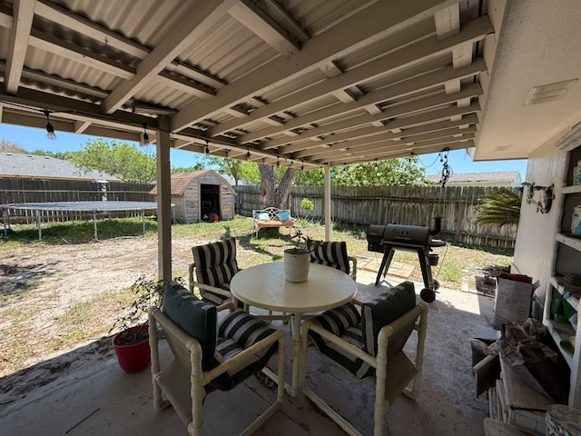 view of patio / terrace with outdoor dining space, a trampoline, an outdoor structure, a fenced backyard, and a storage shed