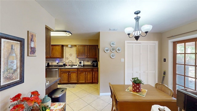 kitchen with light tile patterned floors, decorative light fixtures, a sink, brown cabinets, and decorative backsplash