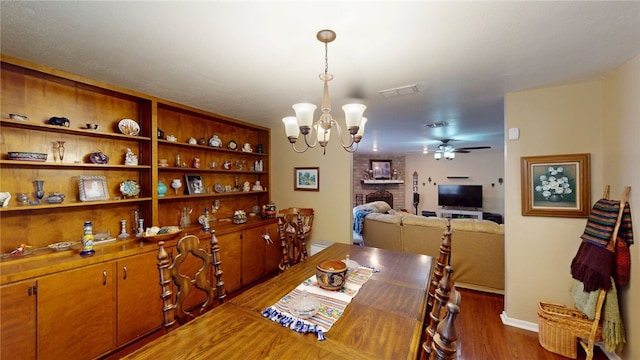 dining space with baseboards, a brick fireplace, visible vents, ceiling fan with notable chandelier, and wood finished floors