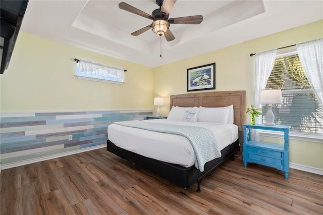 bedroom with ceiling fan, a raised ceiling, and wood-type flooring