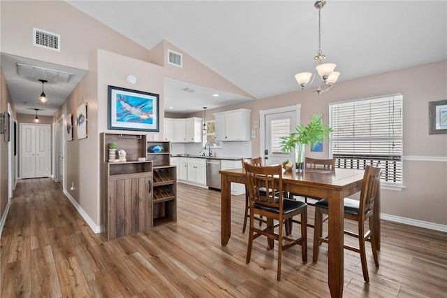 dining room featuring a chandelier, lofted ceiling, sink, and light hardwood / wood-style flooring