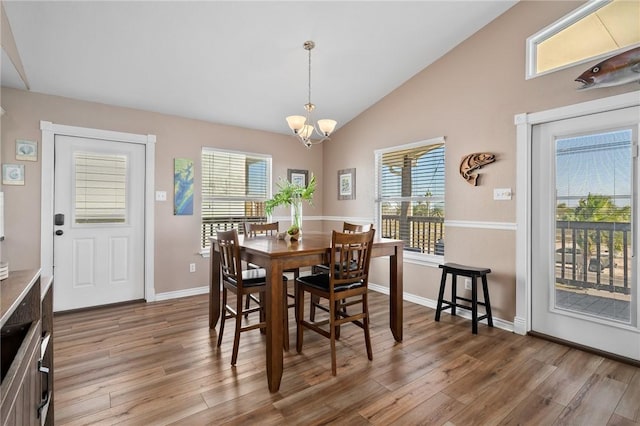 dining room with hardwood / wood-style floors, vaulted ceiling, and a notable chandelier