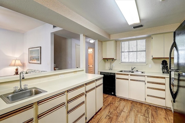 kitchen with a textured ceiling, light hardwood / wood-style flooring, black appliances, and sink