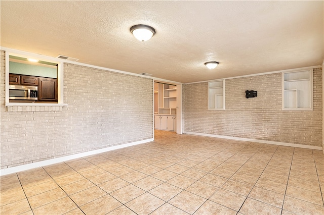 tiled empty room with a textured ceiling and brick wall