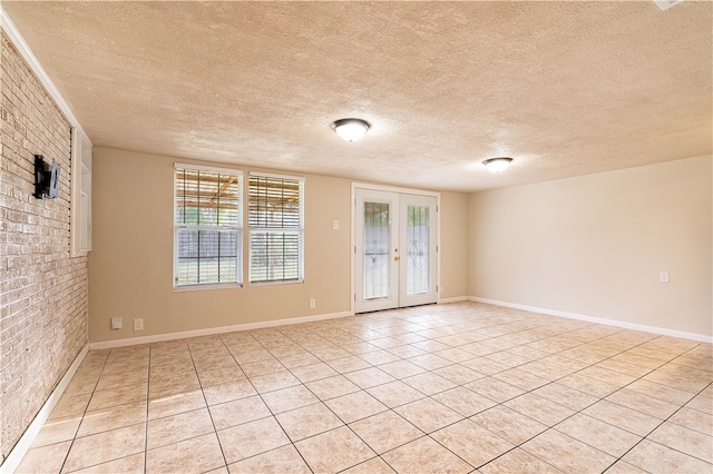 spare room featuring brick wall, a textured ceiling, light tile patterned flooring, and french doors