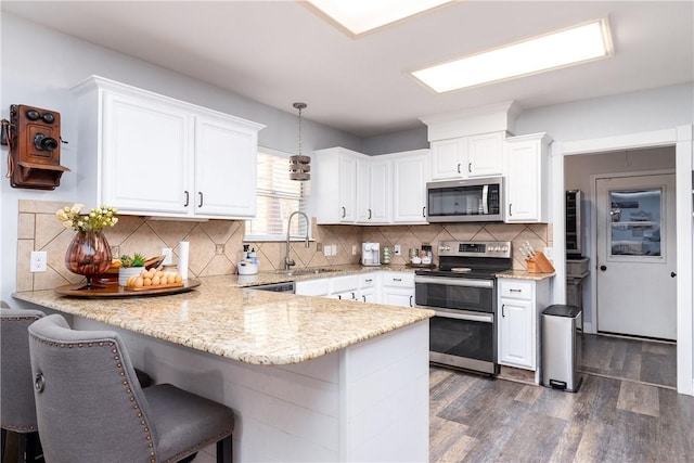 kitchen with stainless steel appliances, white cabinetry, a sink, and a peninsula