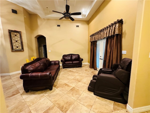 tiled living room with a towering ceiling, ceiling fan, and a raised ceiling