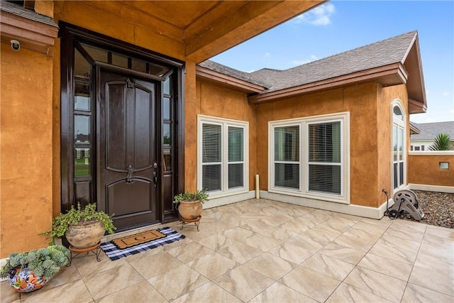 entrance to property with roof with shingles and stucco siding