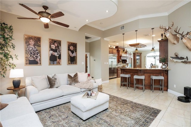 living room featuring light tile patterned flooring, a ceiling fan, visible vents, baseboards, and ornamental molding