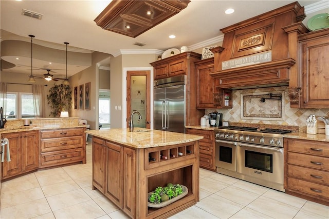 kitchen featuring light stone counters, premium appliances, a kitchen island with sink, visible vents, and brown cabinetry