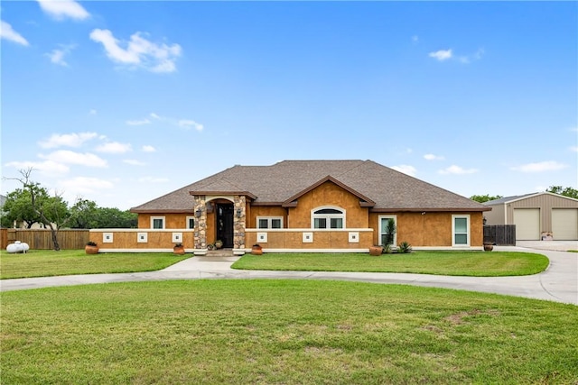 view of front of house with a shingled roof, a detached garage, fence, stone siding, and a front yard