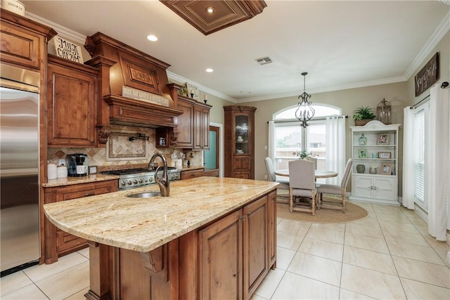 kitchen featuring built in fridge, brown cabinets, a center island with sink, visible vents, and light stone countertops