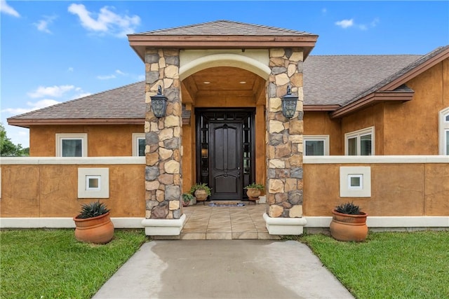 view of exterior entry featuring stone siding, roof with shingles, and stucco siding