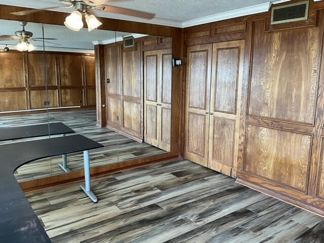 interior space featuring ceiling fan, dark hardwood / wood-style floors, wooden walls, and crown molding