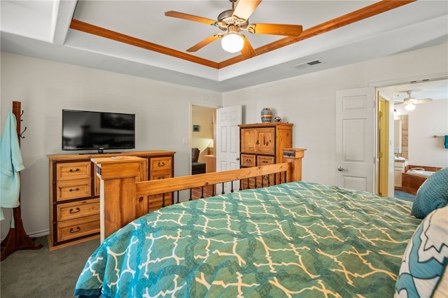 bedroom featuring a tray ceiling, dark carpet, ceiling fan, and ensuite bathroom