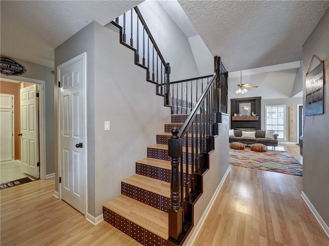 stairs featuring a fireplace, hardwood / wood-style flooring, a textured ceiling, and vaulted ceiling