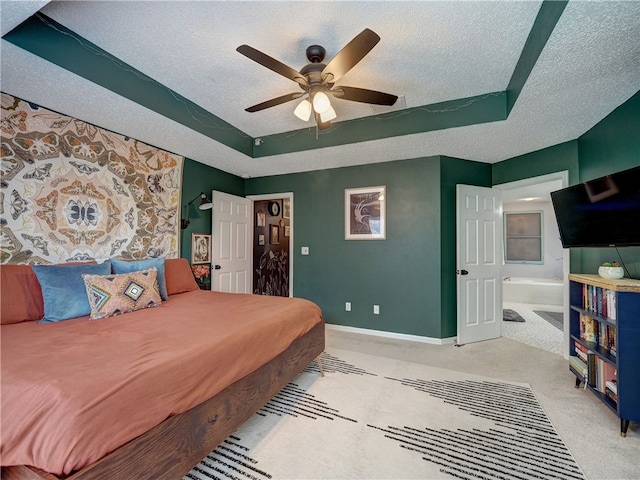 bedroom with a textured ceiling, light carpet, ensuite bathroom, ceiling fan, and a tray ceiling