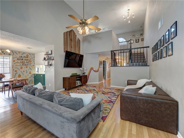 living room featuring a textured ceiling, hardwood / wood-style floors, ceiling fan with notable chandelier, and a towering ceiling