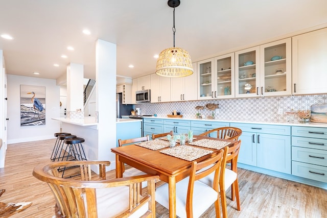 kitchen with backsplash, white cabinets, blue cabinetry, decorative light fixtures, and stainless steel appliances