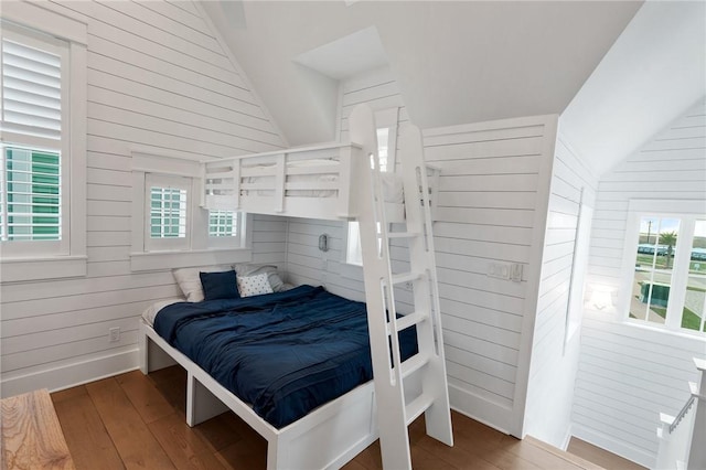 bedroom with vaulted ceiling, hardwood / wood-style flooring, baseboards, and wood walls